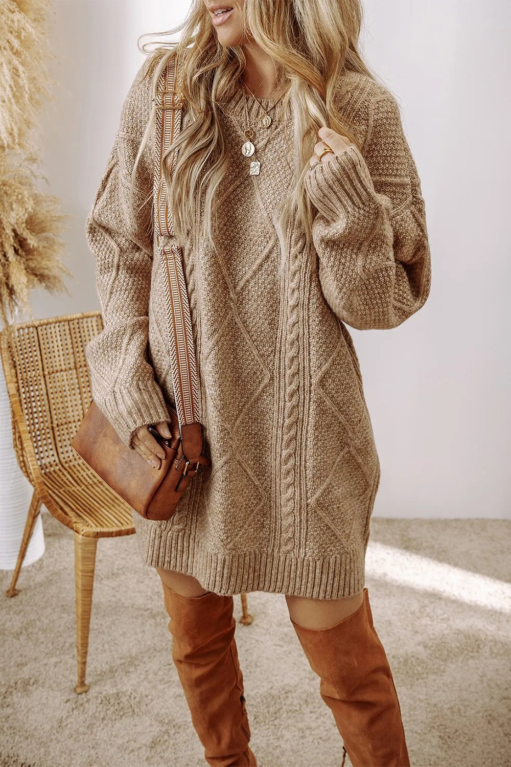 Tan cable-knit sweater dress with round neck and long sleeves, styled with knee-high brown boots and a small brown crossbody .