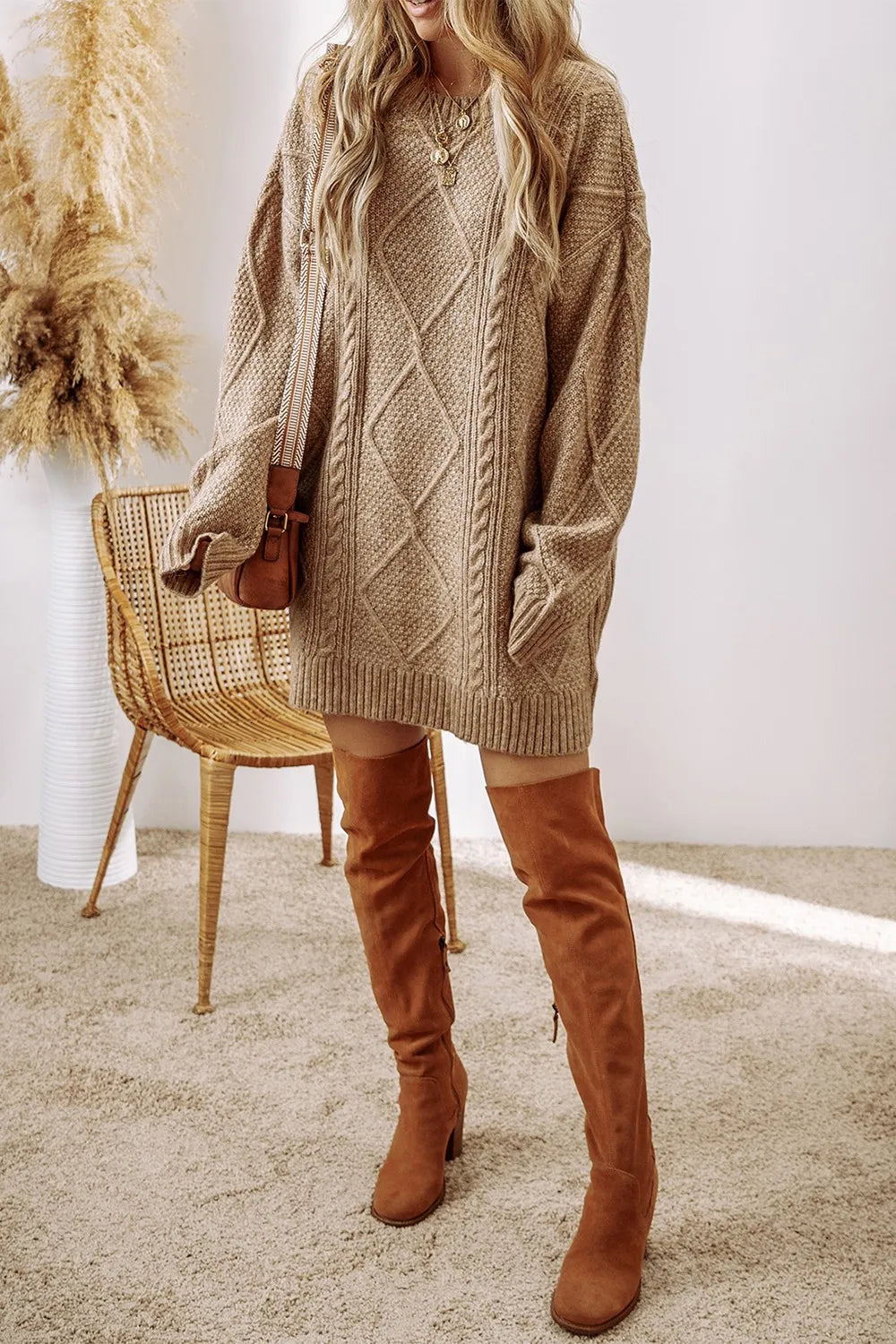 Tan cable-knit sweater dress with round neck and long sleeves styled with knee-high brown suede boots.