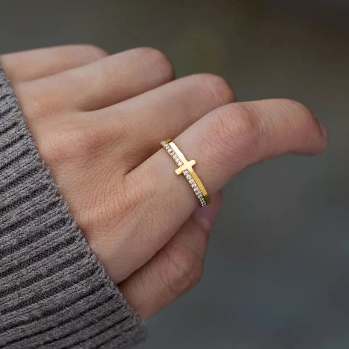 Gold sterling silver ring with horizontal cross and small embedded crystals on finger.