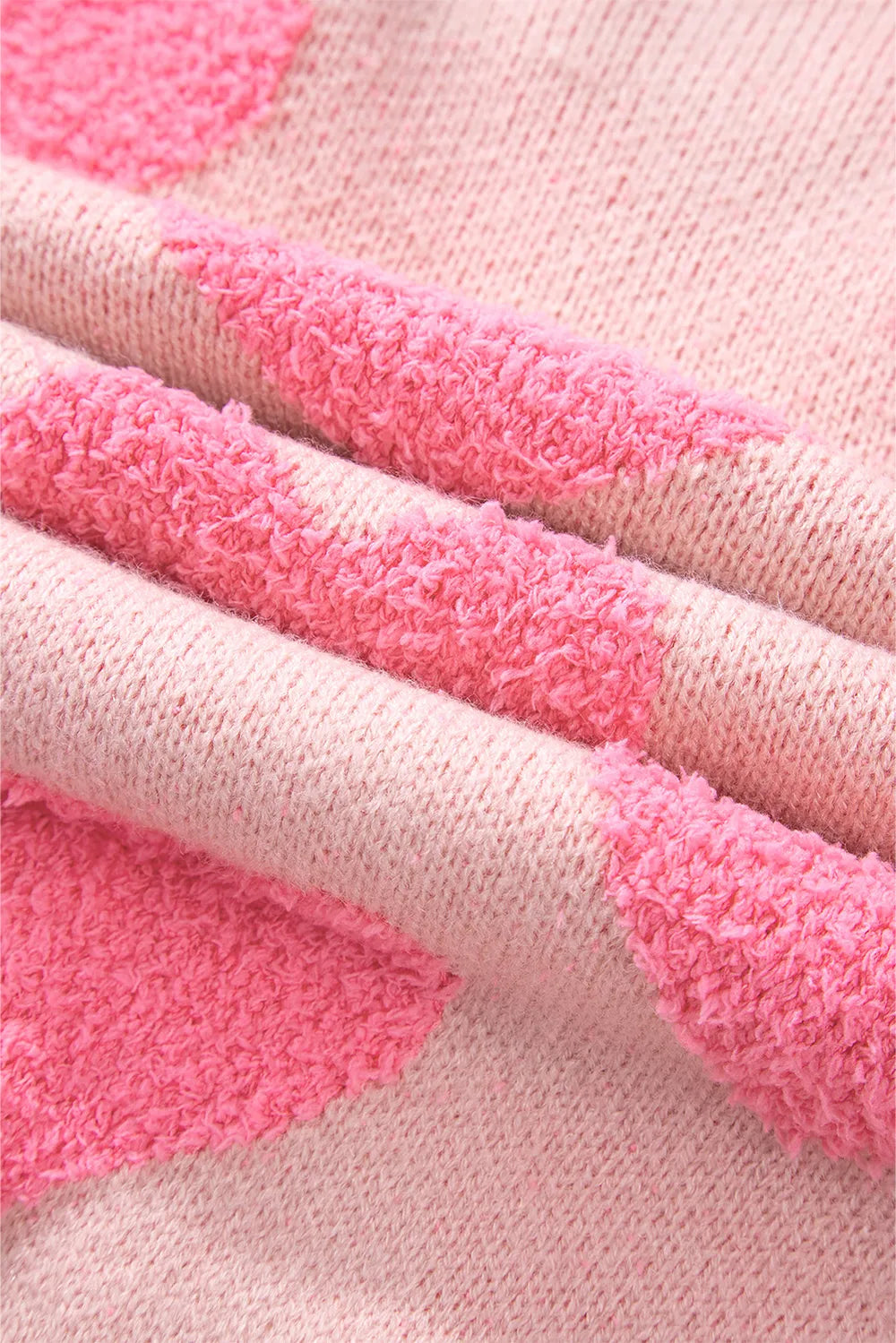 Blush pink knit sweater with raised heart jacquard pattern and round neckline close-up detail.