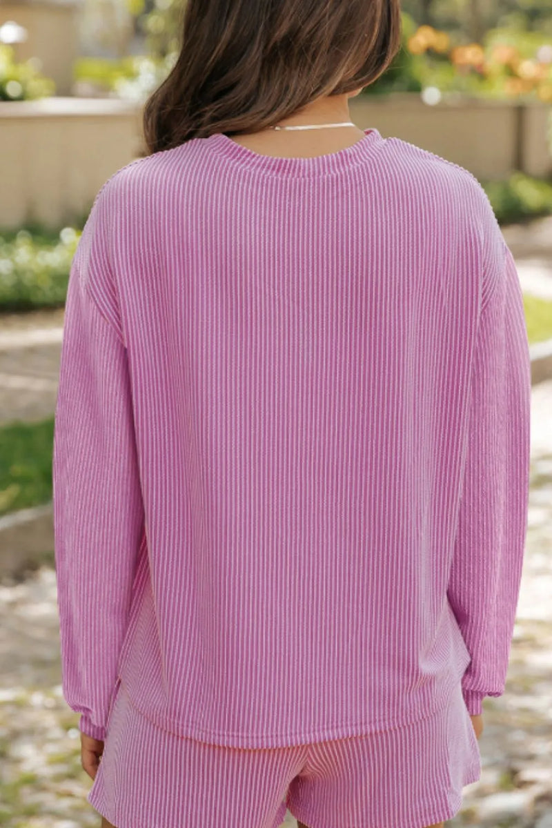 Pink long-sleeve ribbed top with relaxed fit, paired with matching shorts, worn outdoors.