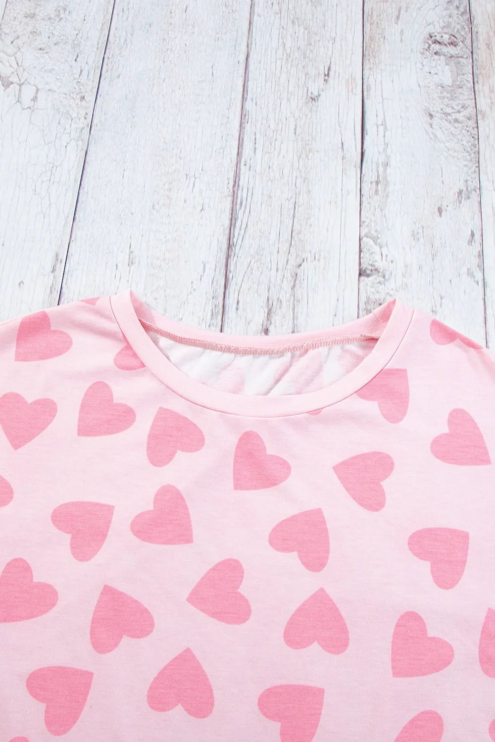 Blush pink long sleeve top with scattered darker pink heart prints and a round neckline.