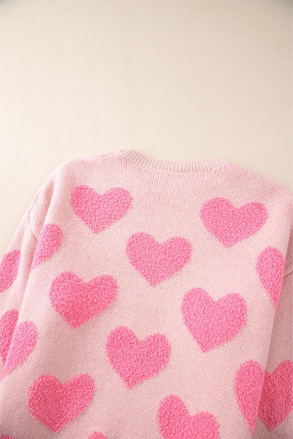 Blush pink sweater with round neck and large bright pink jacquard hearts pattern on back.