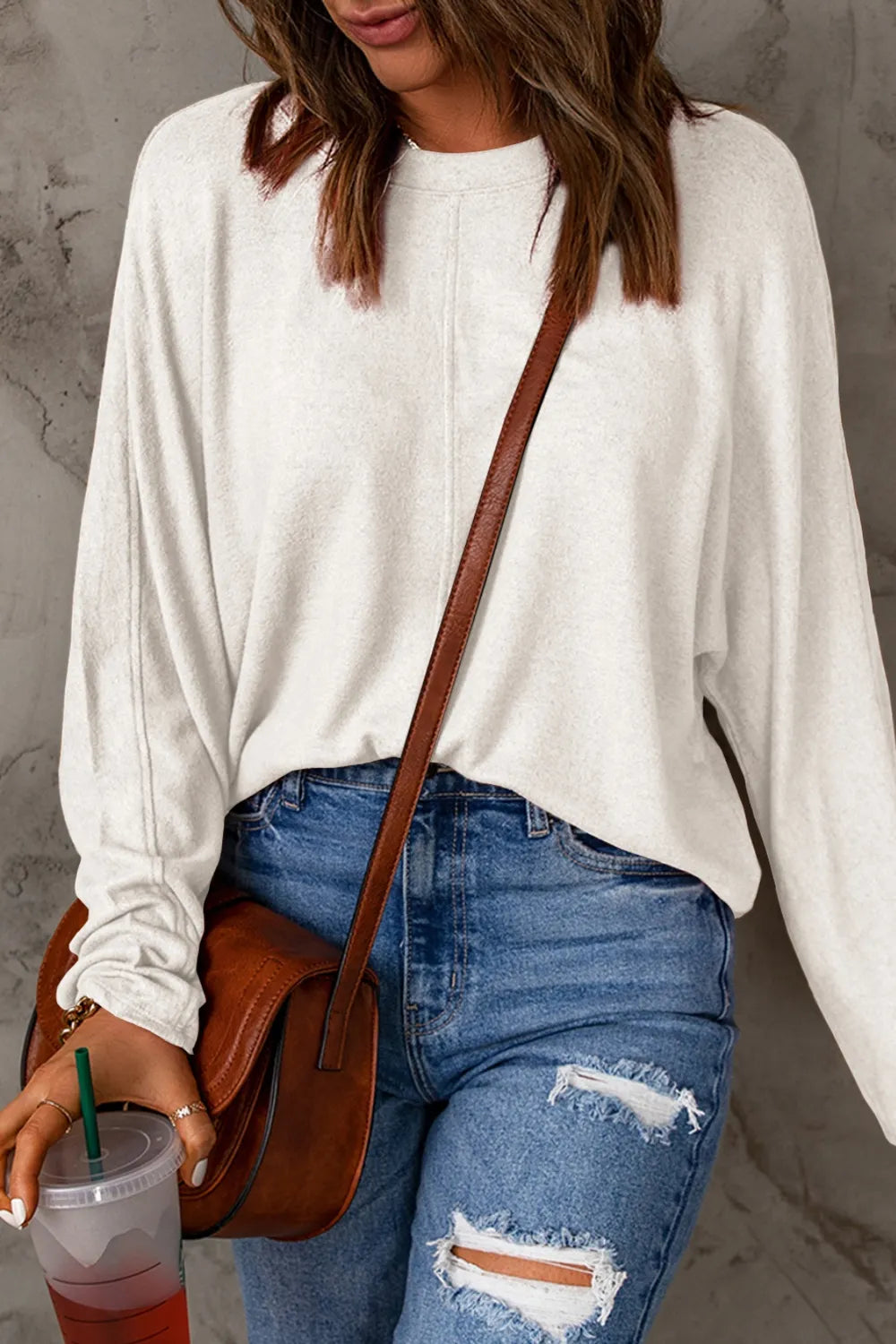 White full sleeve round neck t-shirt paired with ripped blue jeans and a brown crossbody bag.