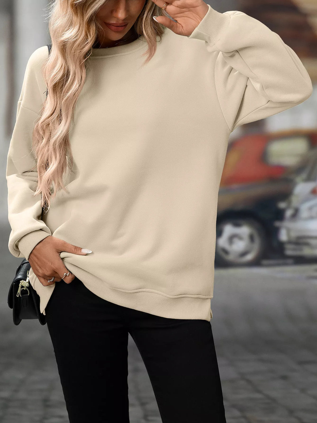 Beige casual long sleeve sweatshirt with relaxed fit and ribbed cuffs worn with black pants.