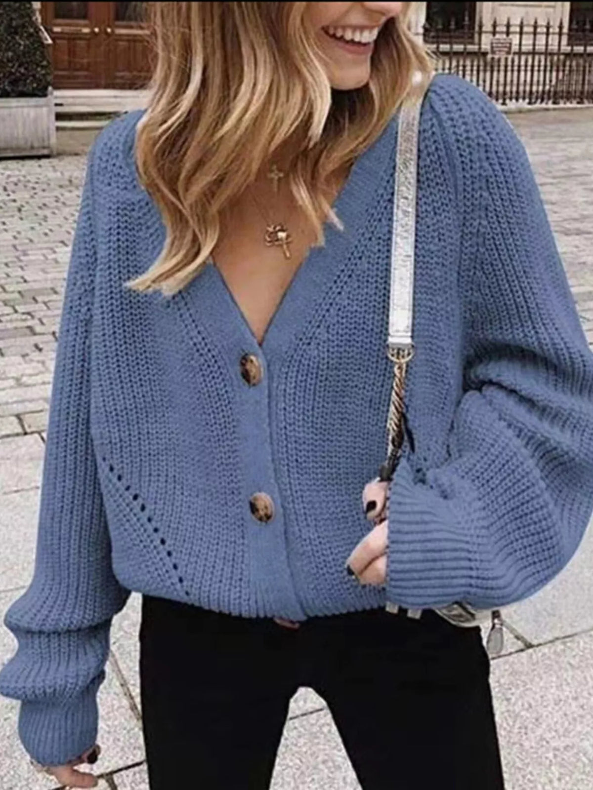 Blue chunky knit cardigan with large buttons and balloon sleeves worn over black pants.