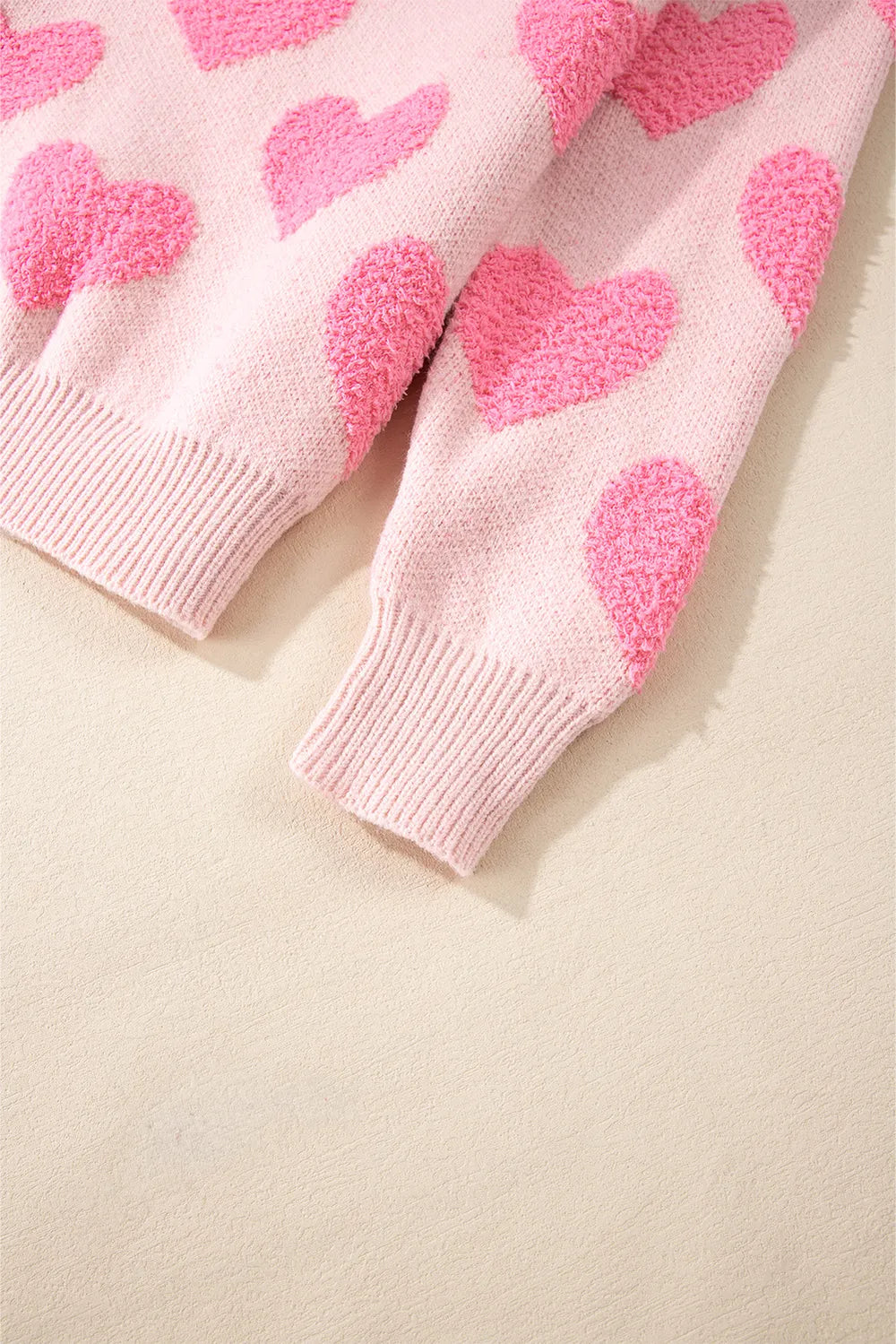 Blush pink sweater sleeves with textured bright pink jacquard hearts and ribbed cuffs.