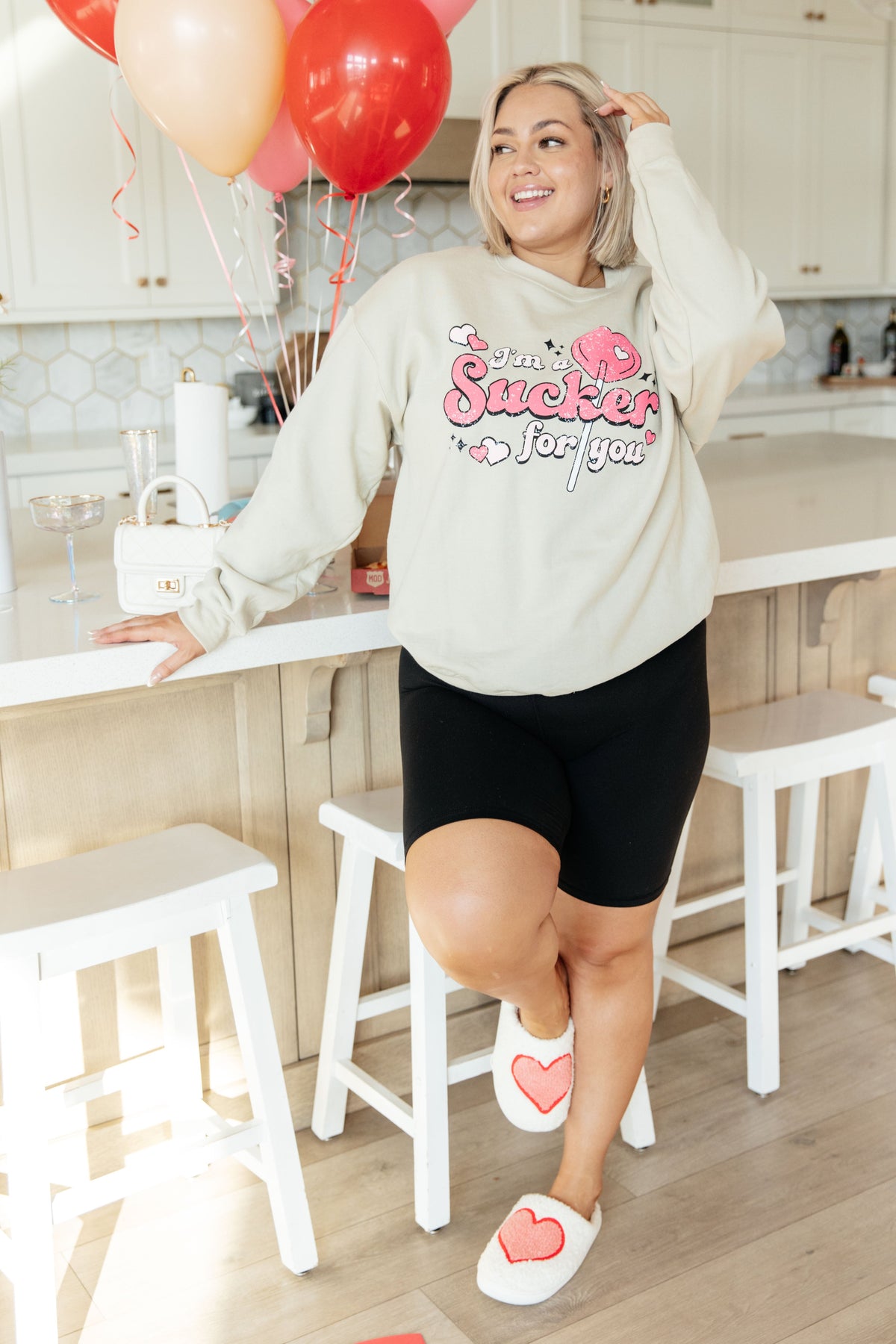 Cream pullover sweatshirt with pink and red "I'm A Sucker For You" Valentine graphic, worn with black shorts and heart.