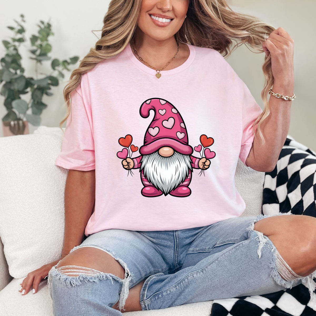 Pink oversized tee with Valentine gnome in heart-patterned hat holding two hearts, worn with ripped jeans.