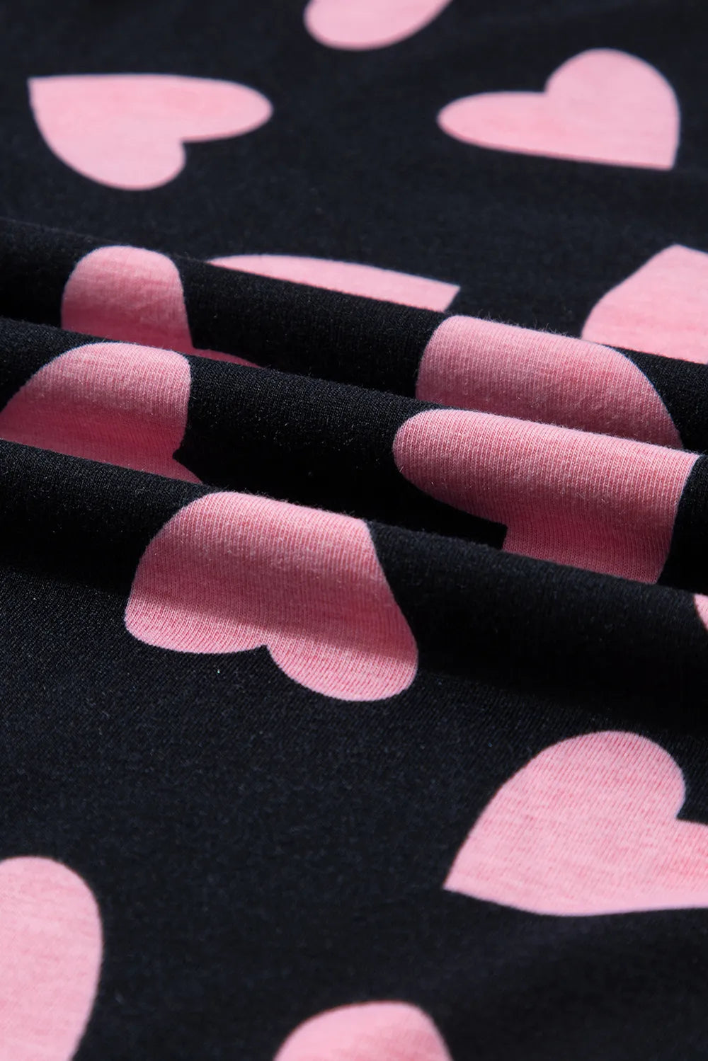 Black fabric with large blush pink heart prints in soft knit material.