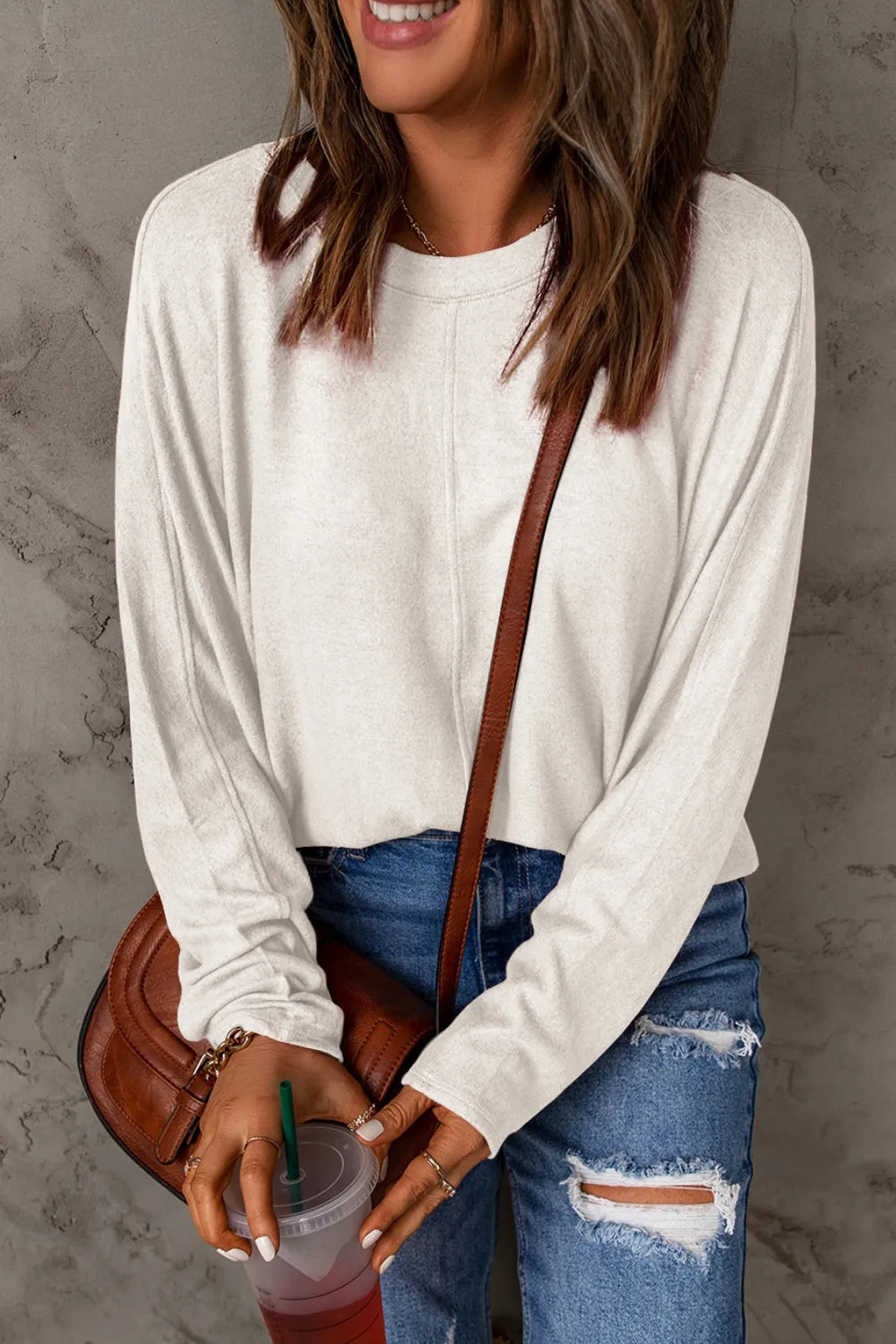 White long sleeve round neck t-shirt with relaxed fit worn with distressed blue jeans and brown crossbody bag.
