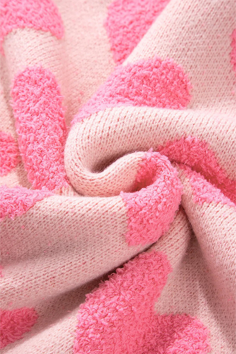 Blush pink knit sweater fabric with raised jacquard heart patterns, soft textured close-up.