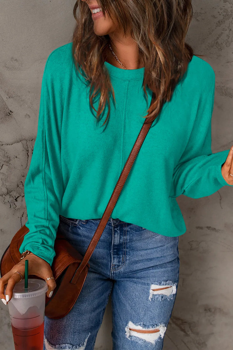 Turquoise long sleeve round neck t-shirt paired with distressed blue jeans and a brown crossbody bag.