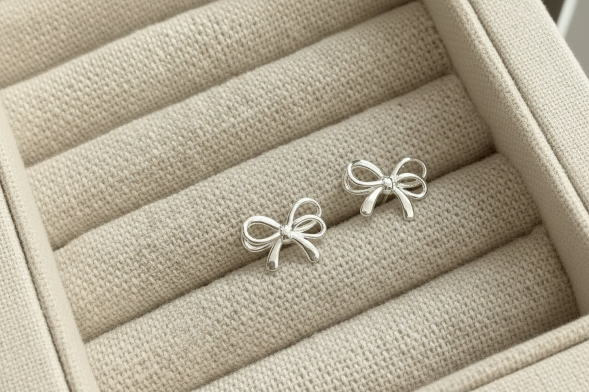 Sterling silver bow-shaped stud earrings on beige jewelry display tray.
