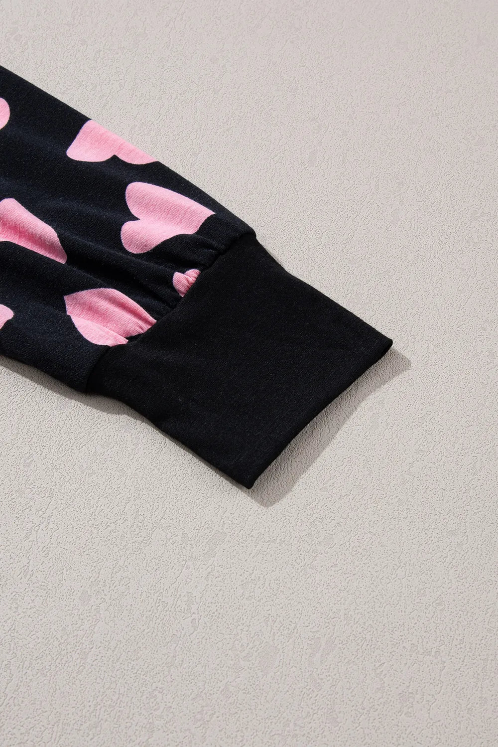 Black long sleeve cuff with pink heart print on fabric above cuff.