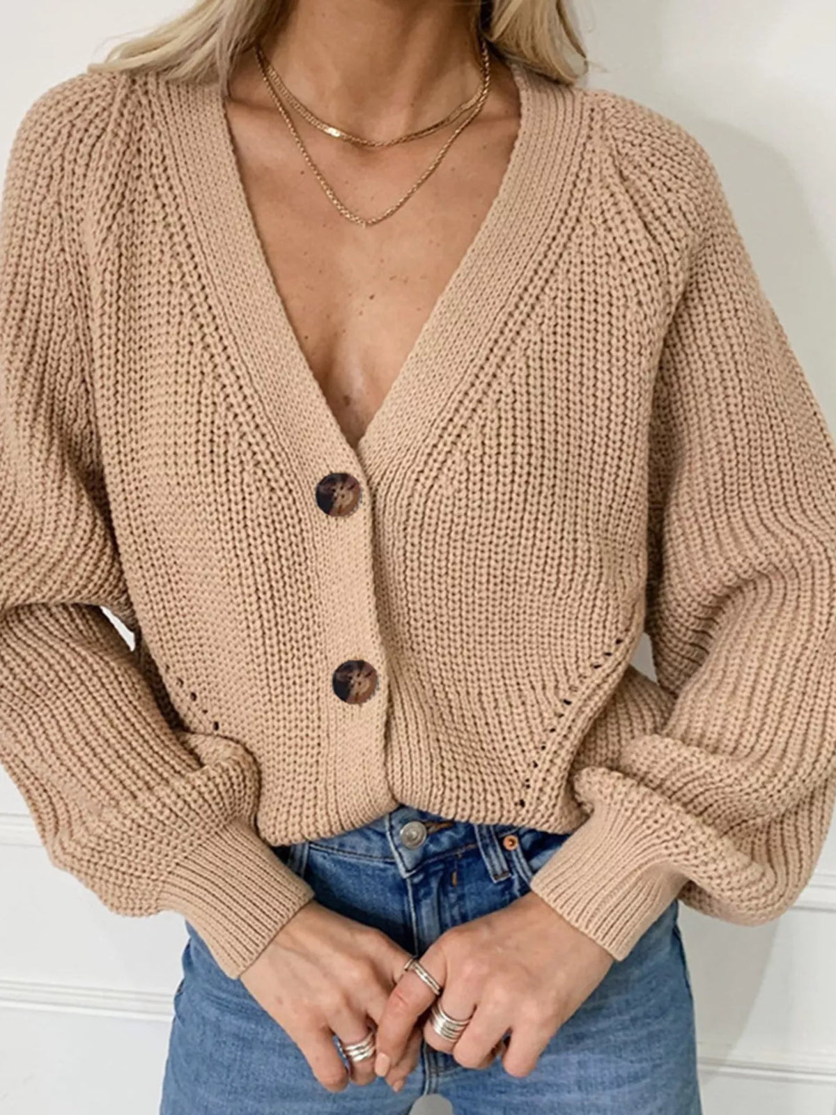 Khaki chunky knit button-down cardigan with balloon sleeves and deep V-neck worn with blue jeans.
