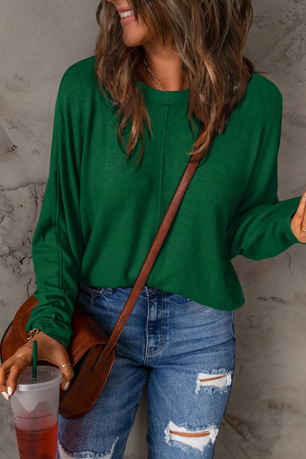 Green long sleeve round neck T-shirt worn with ripped blue jeans and a brown crossbody bag.