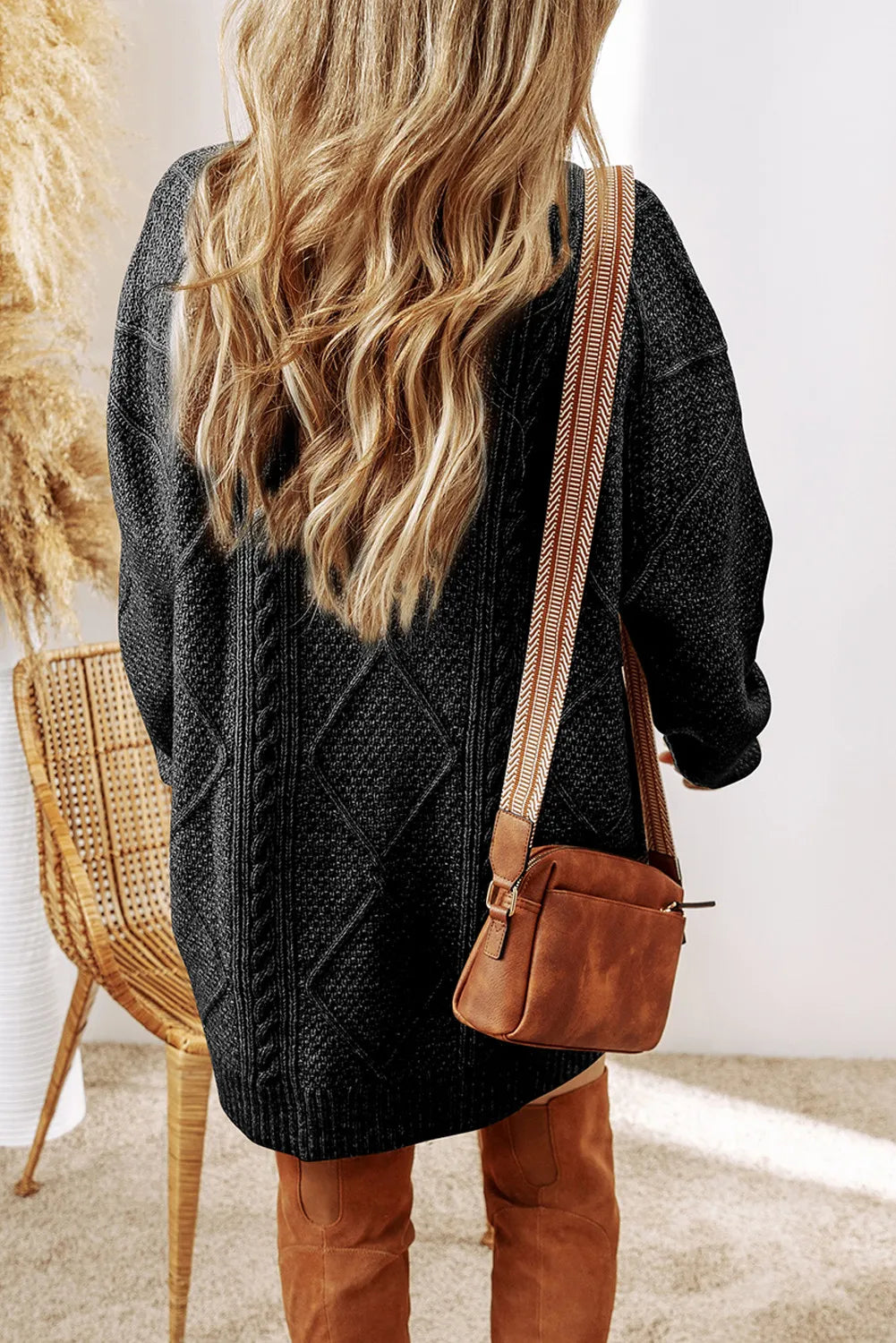 Black cable-knit round neck sweater dress with long sleeves worn with brown suede crossbody bag and tall brown boots.