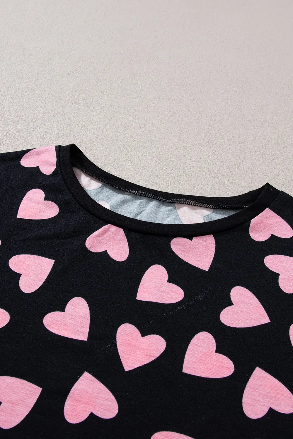 Black long sleeve top with all-over pink heart print and round neckline.