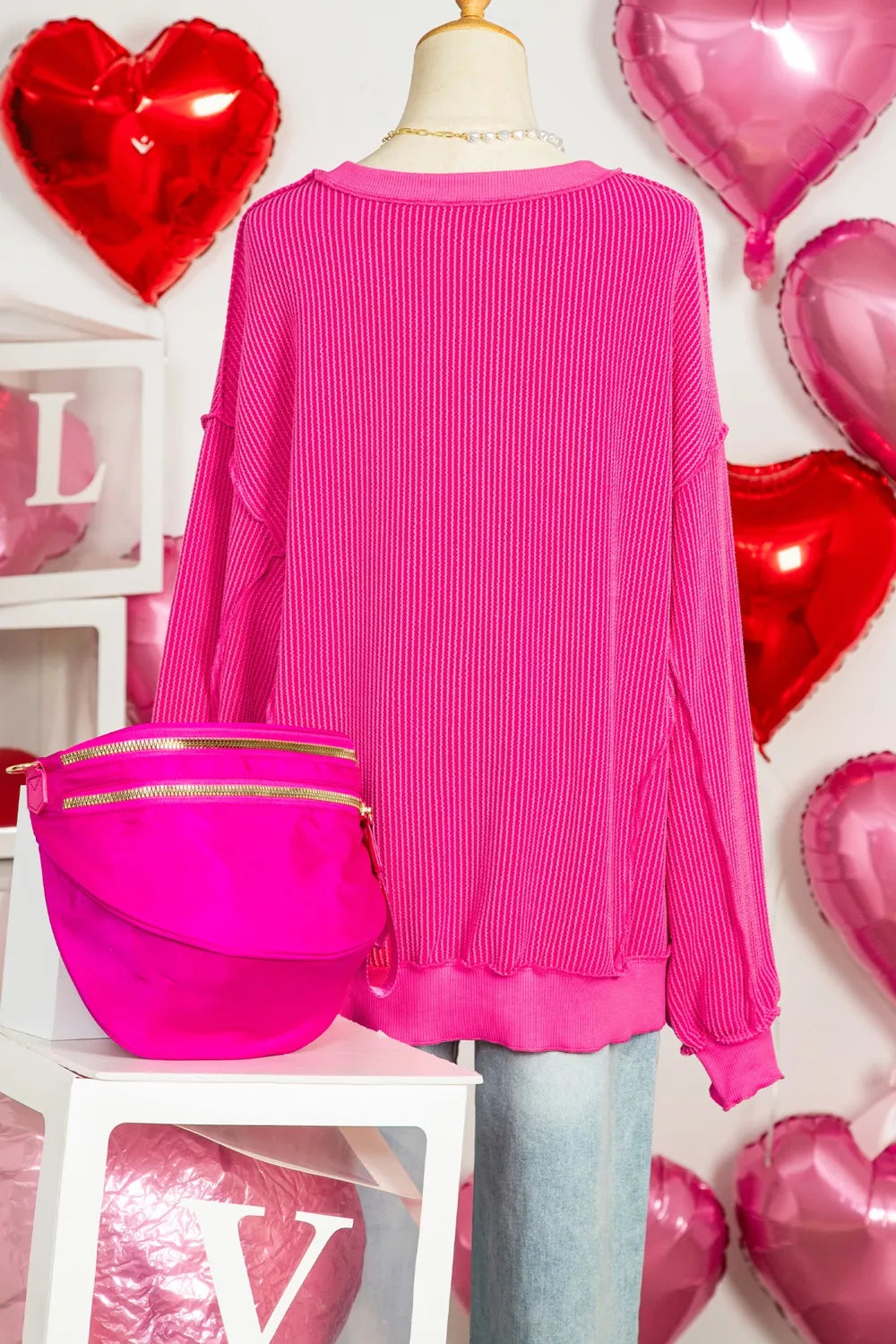 Bright hot pink twisted ribbed long sleeve top on mannequin with light blue jeans and matching pink fanny pack.