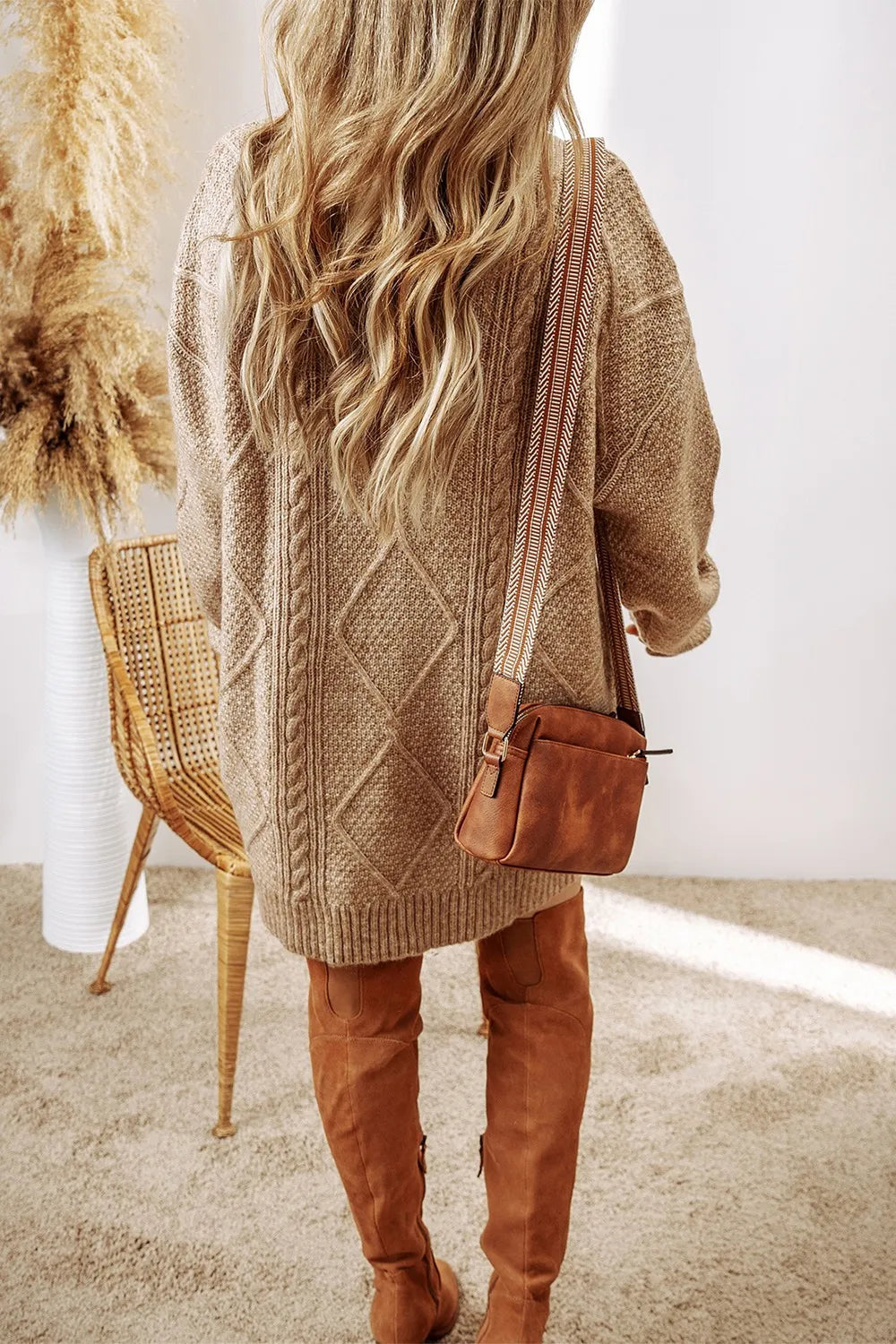 Taupe cable-knit sweater dress with round neck and diamond pattern, styled with brown crossbody bag and over-the-knee boots.